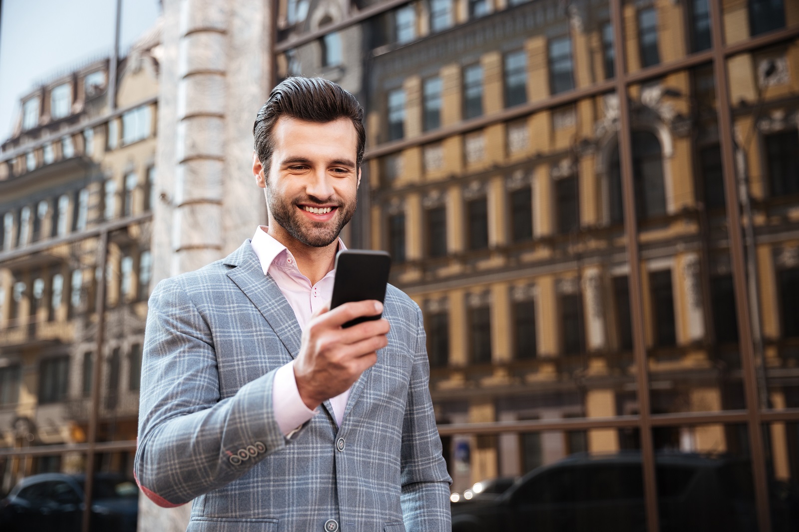 Portrait of a happy handsome man in a jacket looking at mobile phone in a city area