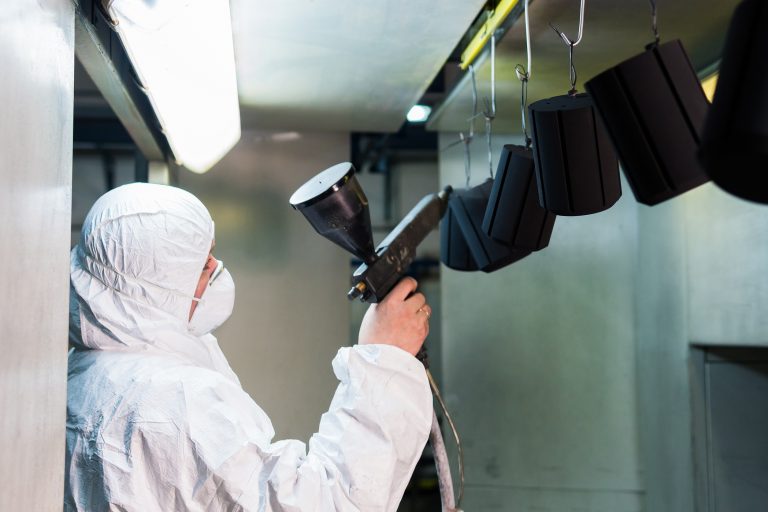 Powder coating of metal parts. A man in a protective suit sprays powder paint from a gun on metal products