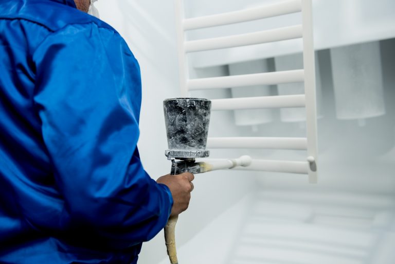 Worker performing powder coating of metal details at metallurgical factory